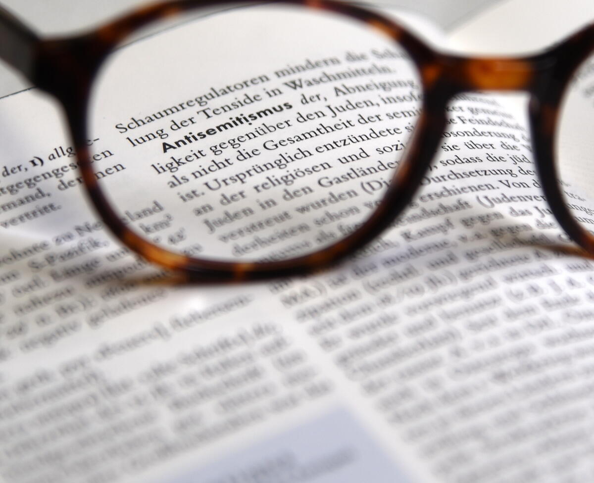 Bild vergrößern: Das Bild zeigt eine Brille auf einem Buch, wo das Wort Antisemitismus hervorsticht