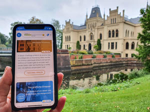 Das Bild zeigt ein Handy, auf dem die App mit einer digitalen Aufgabe zur Geschichte der Evenburg geöffnet ist.