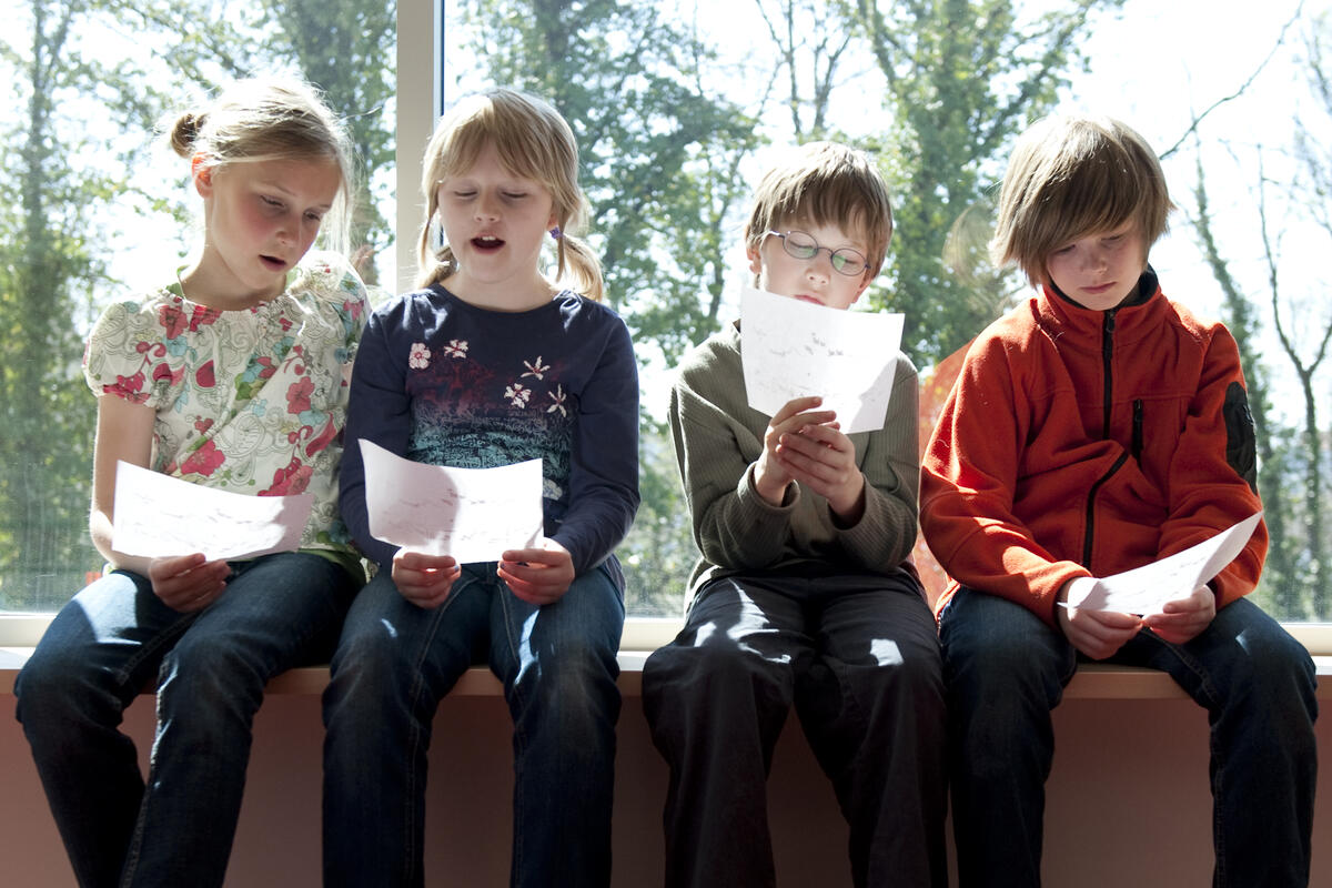 Bild vergrößern: Das Bild zeigt singende Kinder mit Textzetteln in der Hand