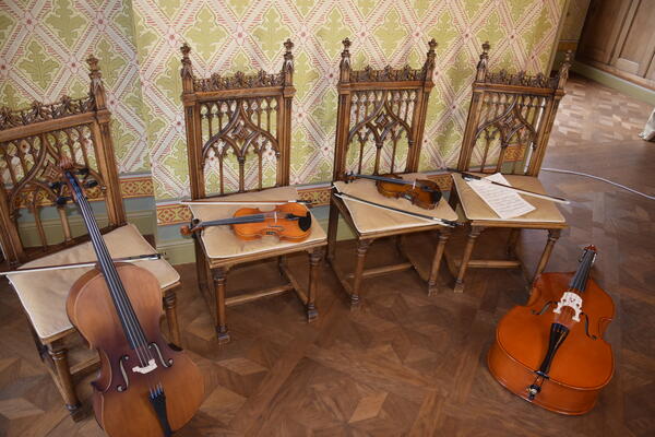 Bild vergrößern: gezeigt werden vier Streichinstrumente auf Stühlen liegend